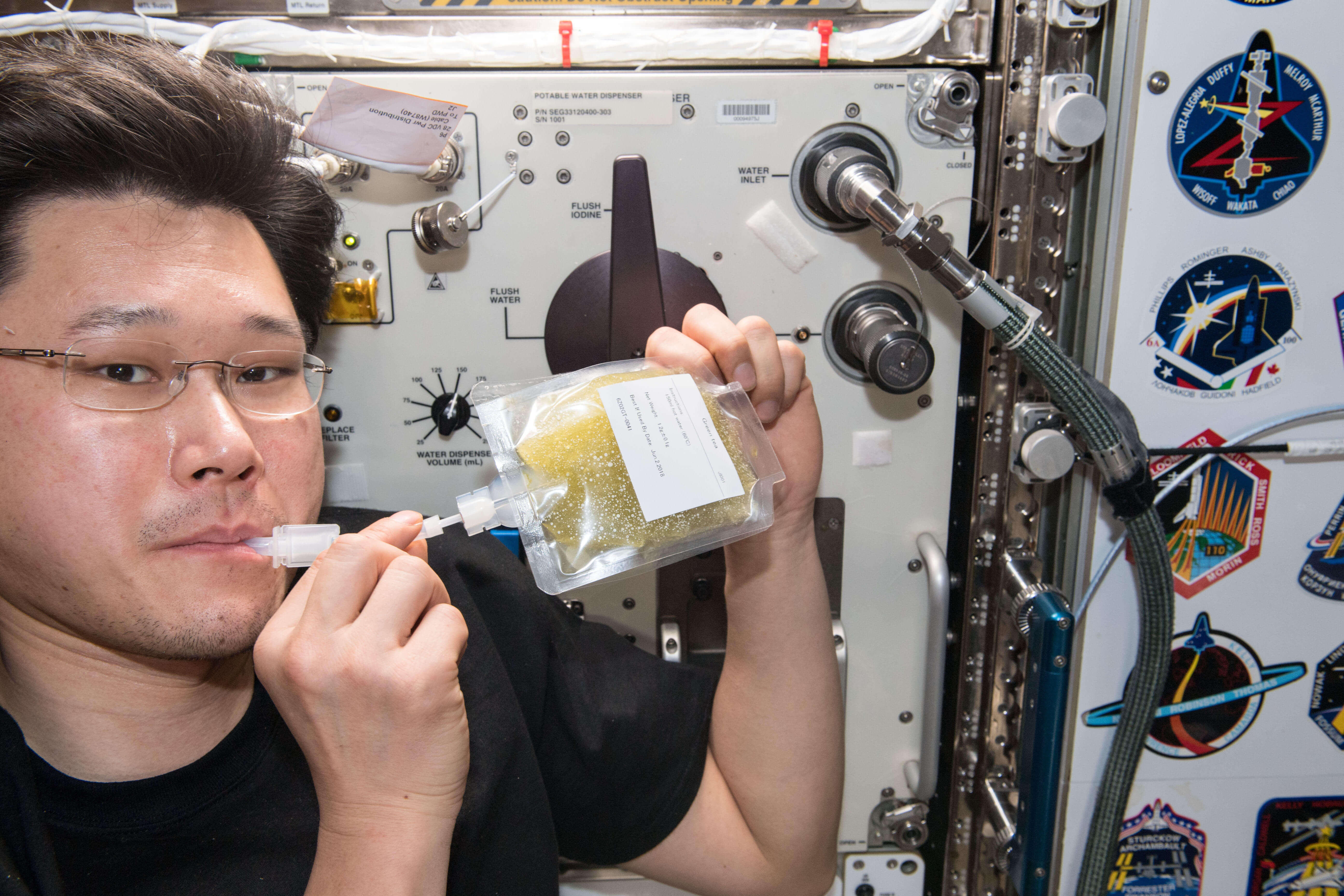 宇宙日本食の緑茶を飲む金井宇宙飛行士。飲みやすいようコンパクトなパッケージに入っている。