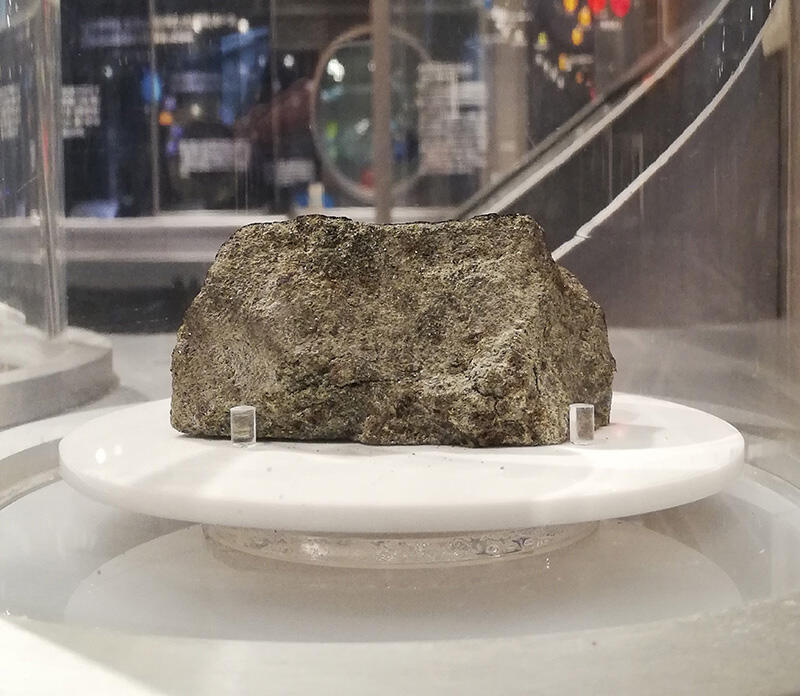 科博・地球館B3階にて展示中の「ナクラ隕石」。長さ約6cm。主に緑がかった輝石という鉱物でできている。