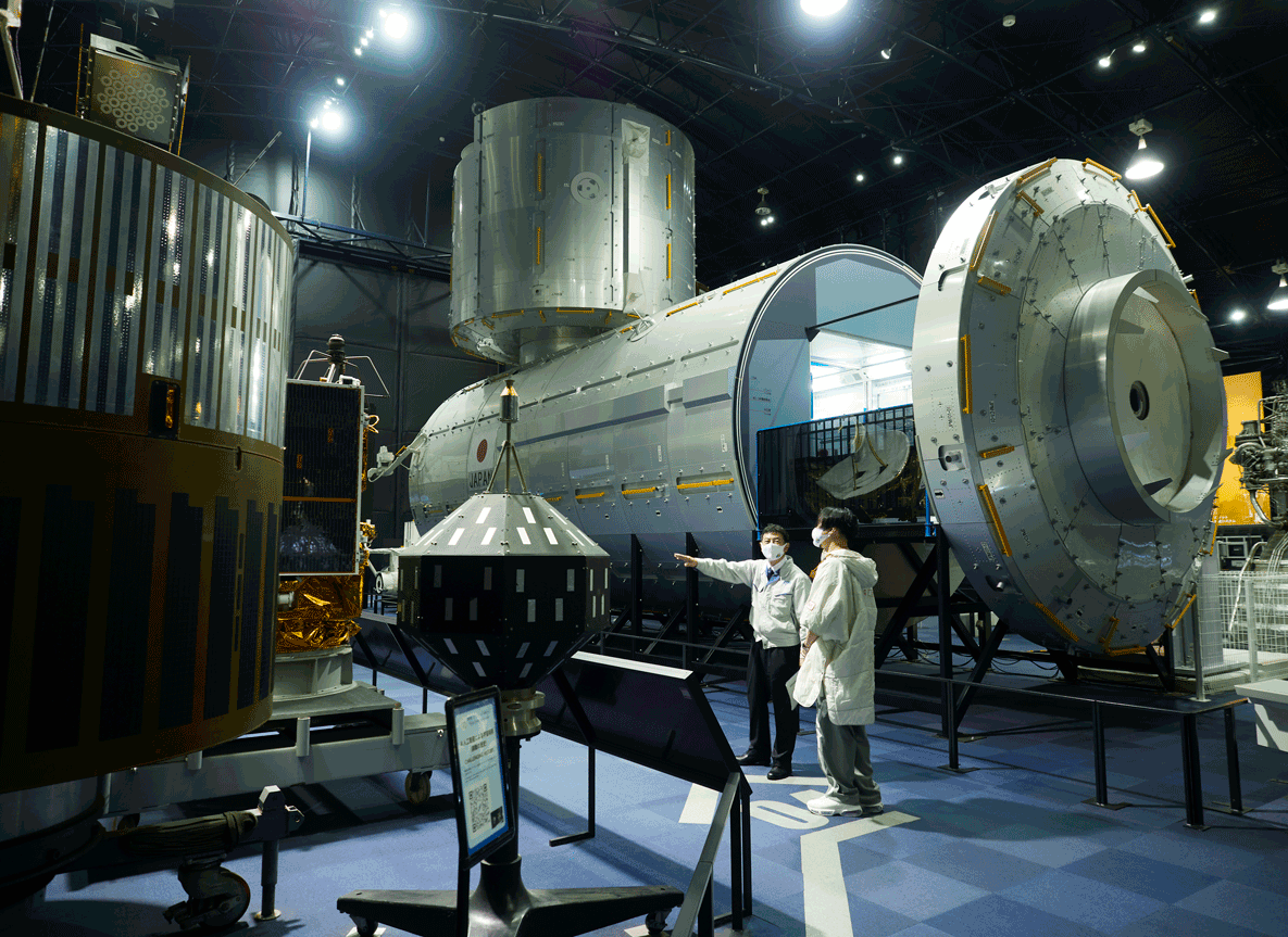 寺田所長の案内のもと、筑波宇宙センター内にある展示館「スペースドーム」で「きく1号」を見学する児玉さん。